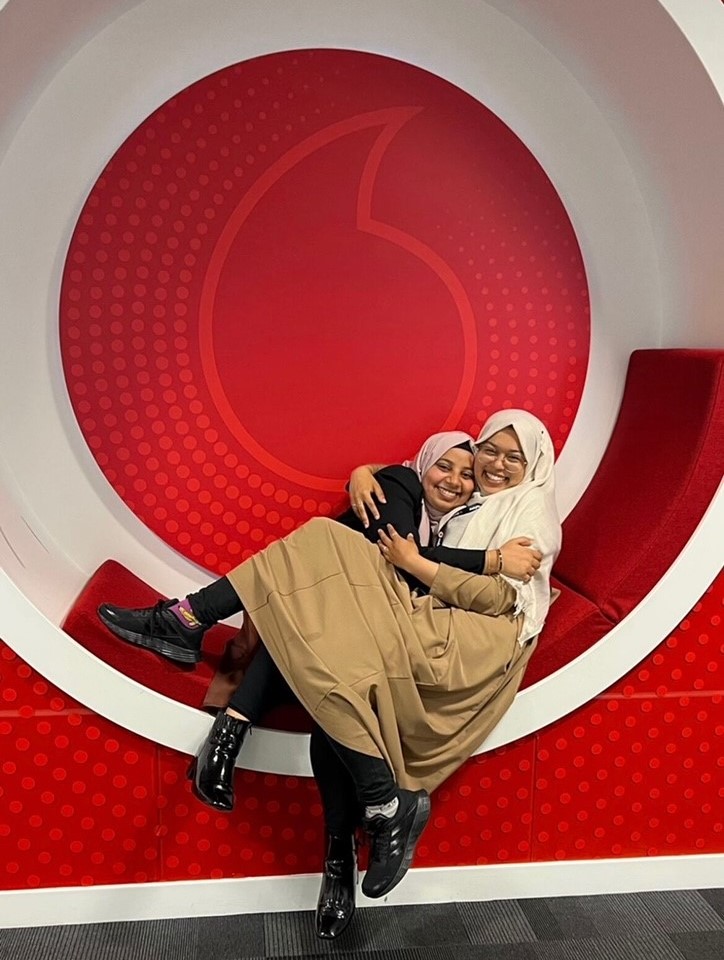 Two friends smiling and hugging in a seat with Vodafone branding