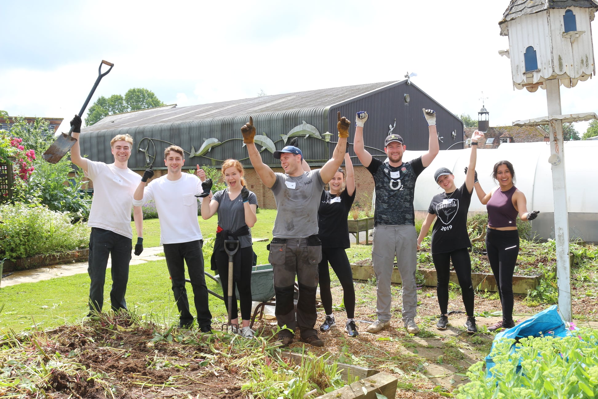A group of people working at a gardening space for a charity day holding equipment