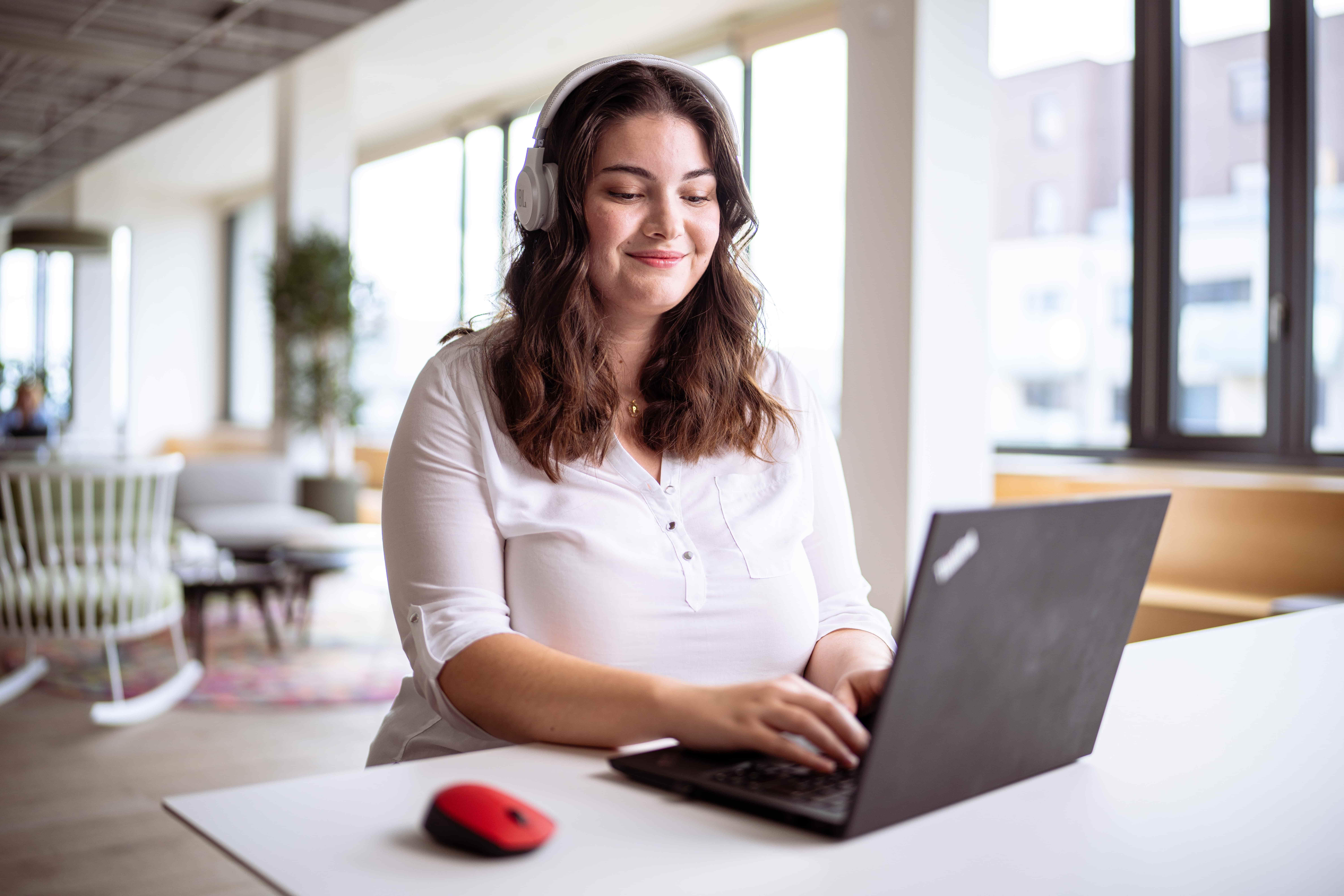 A woman wearing headphones smiling at her laptop sat in the office