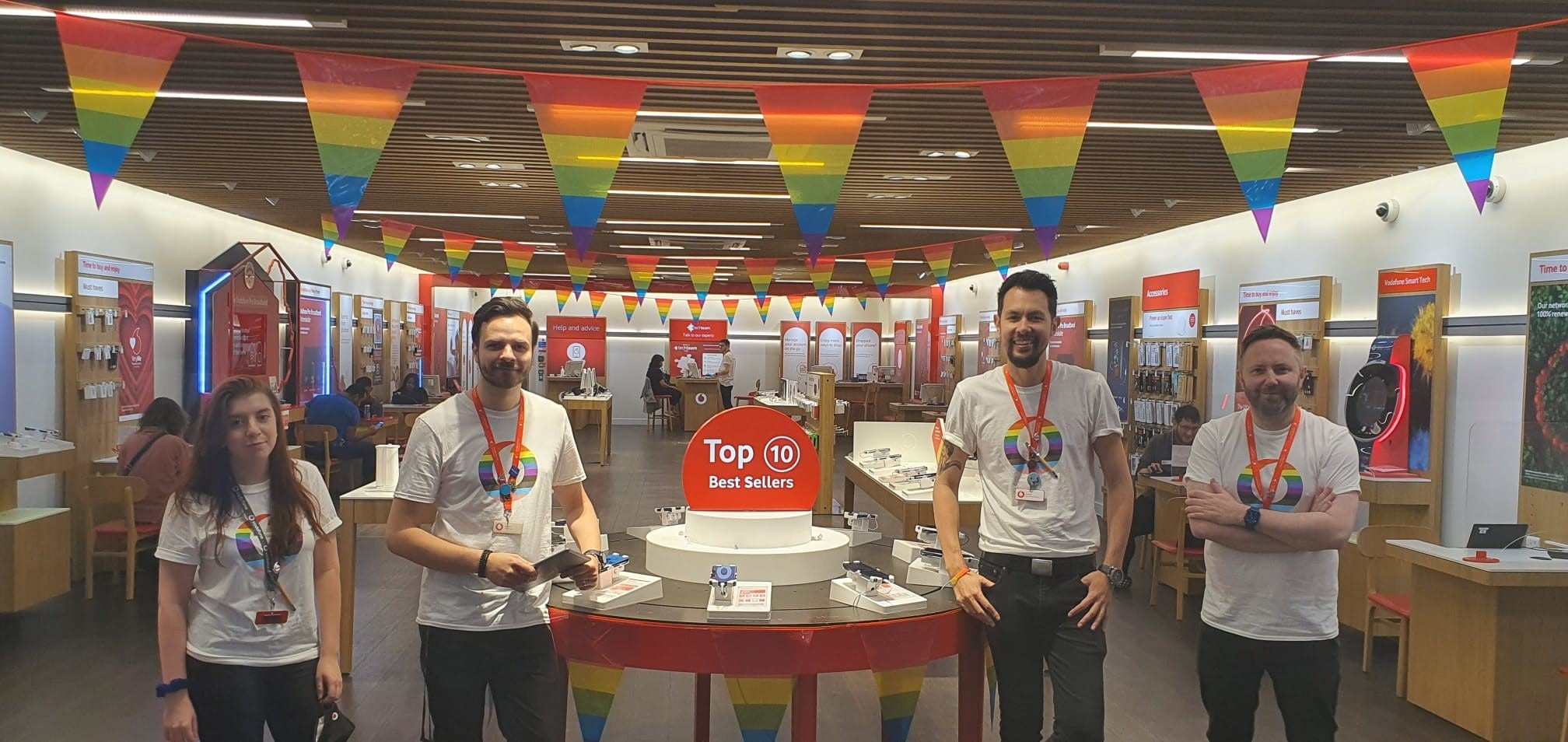 Four people in LGBT vodafone logo tops in retail store with LGBT decorations