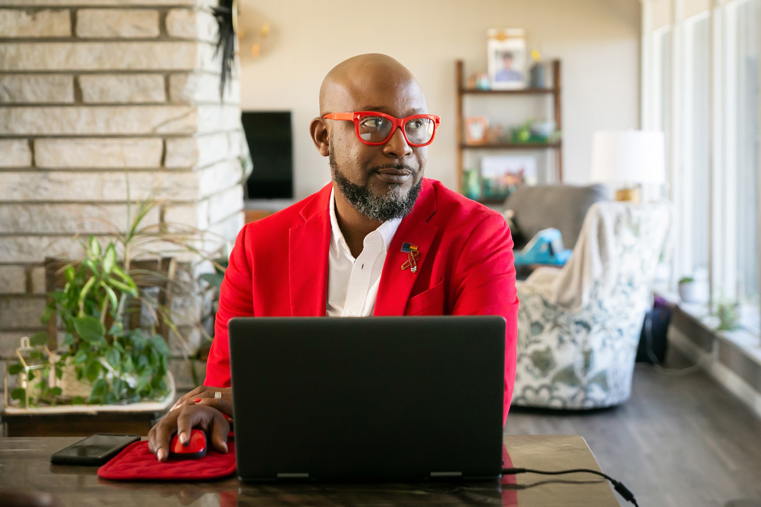 A man sat at a desk with a laptop looking to the right wearing red glasses