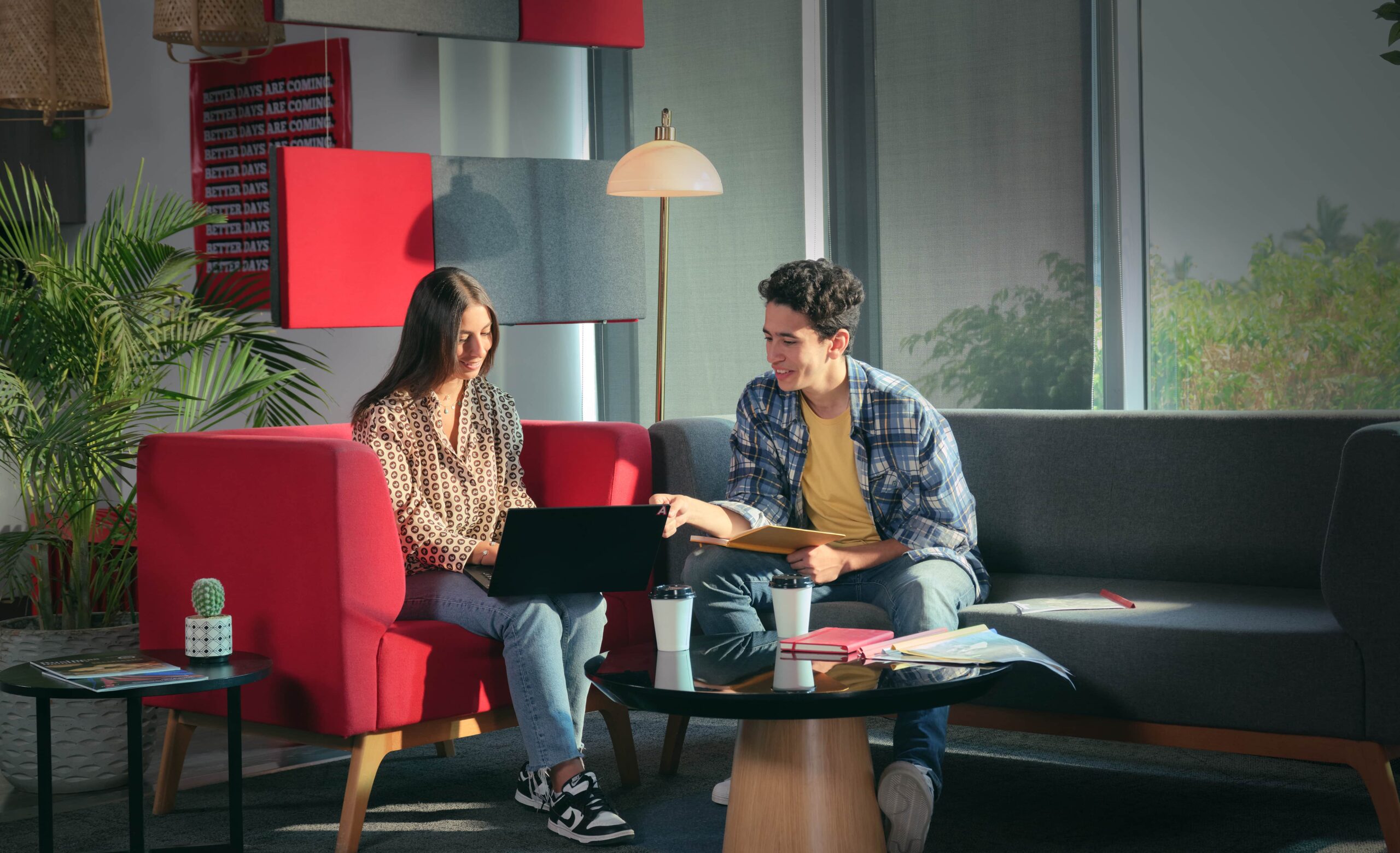 Two people sat on a sofa smiling at a laptop in an office environment