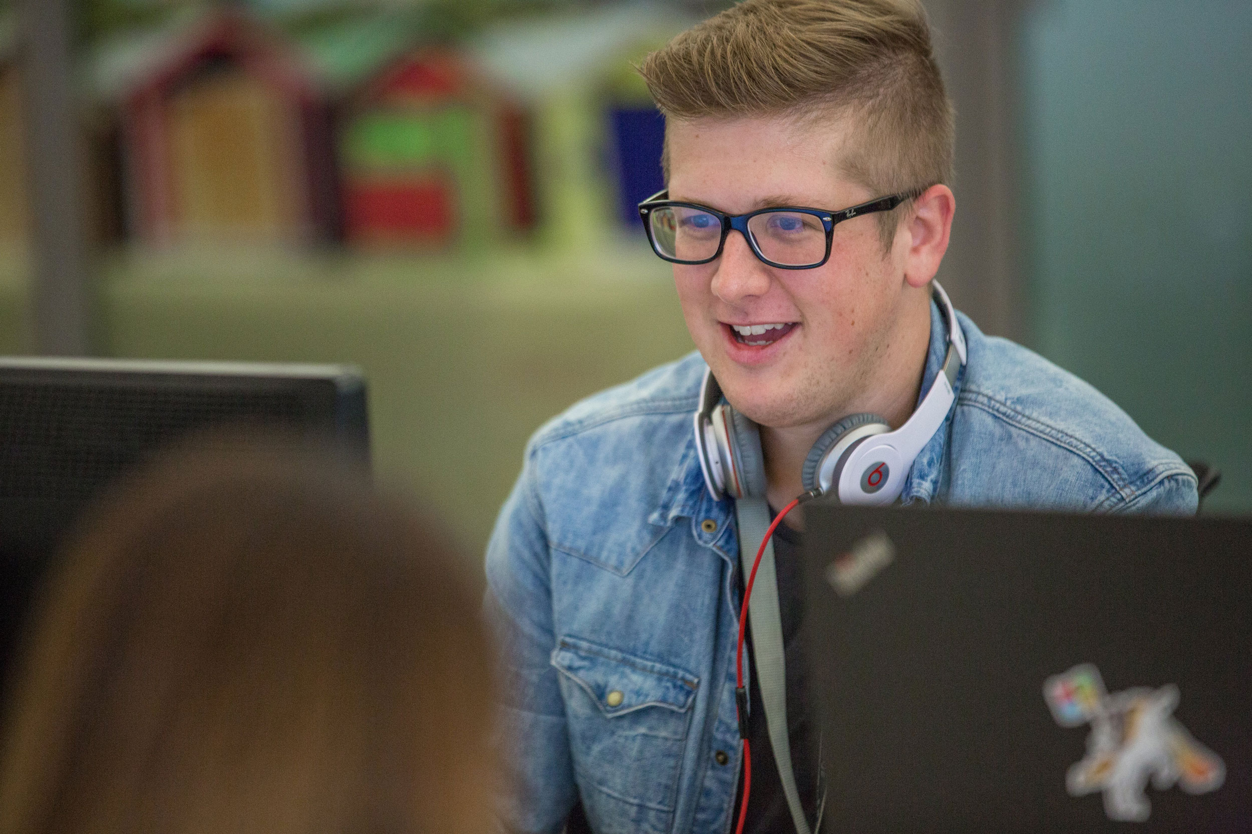 A person sat smiling at his laptop on a desk