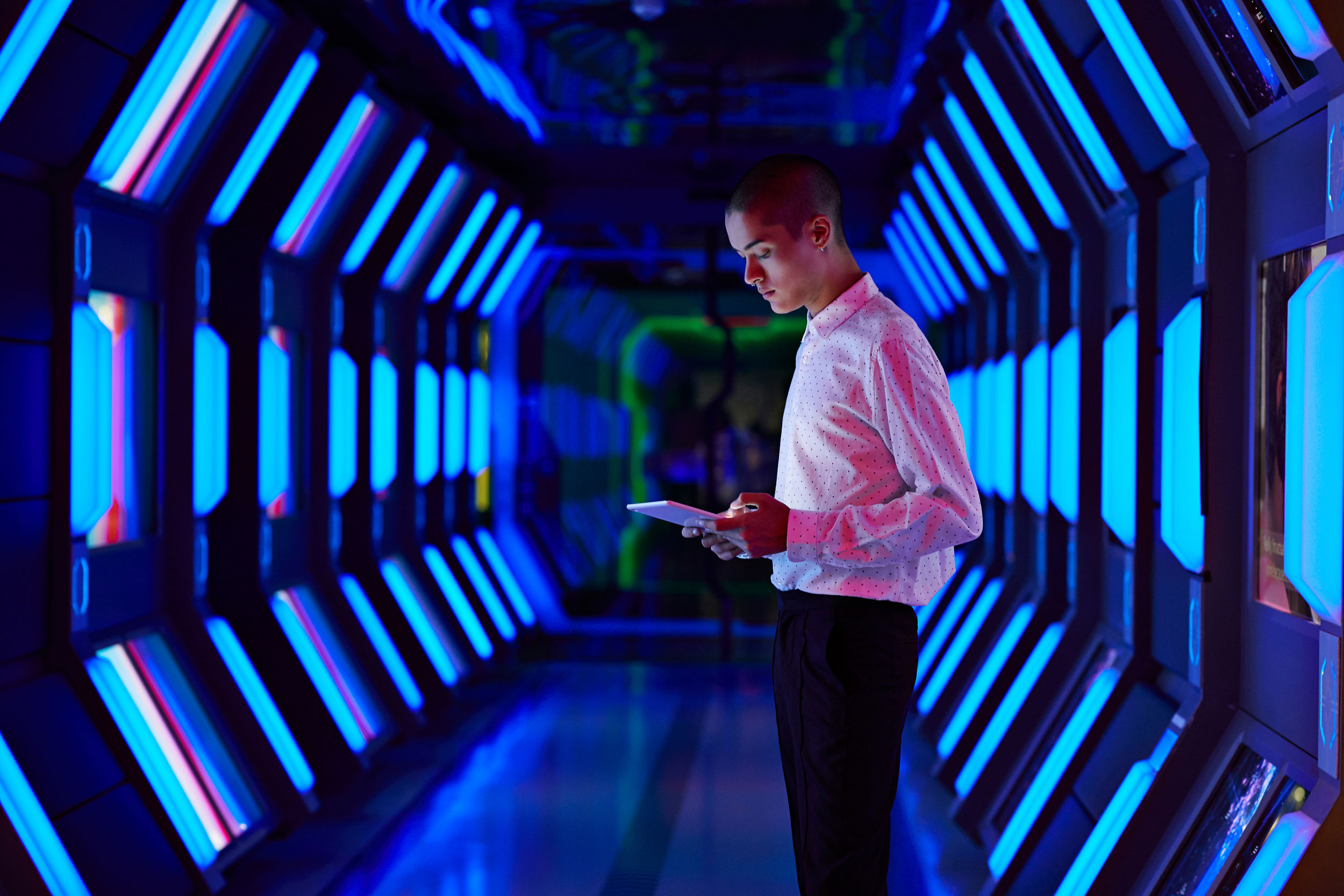 A man in a blue light hallway on his ipad