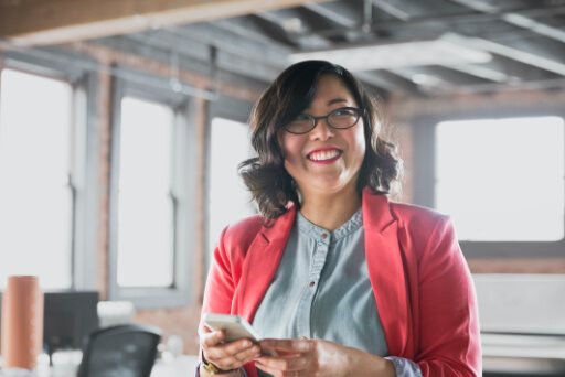 A woman smiling into the distance holding a phone