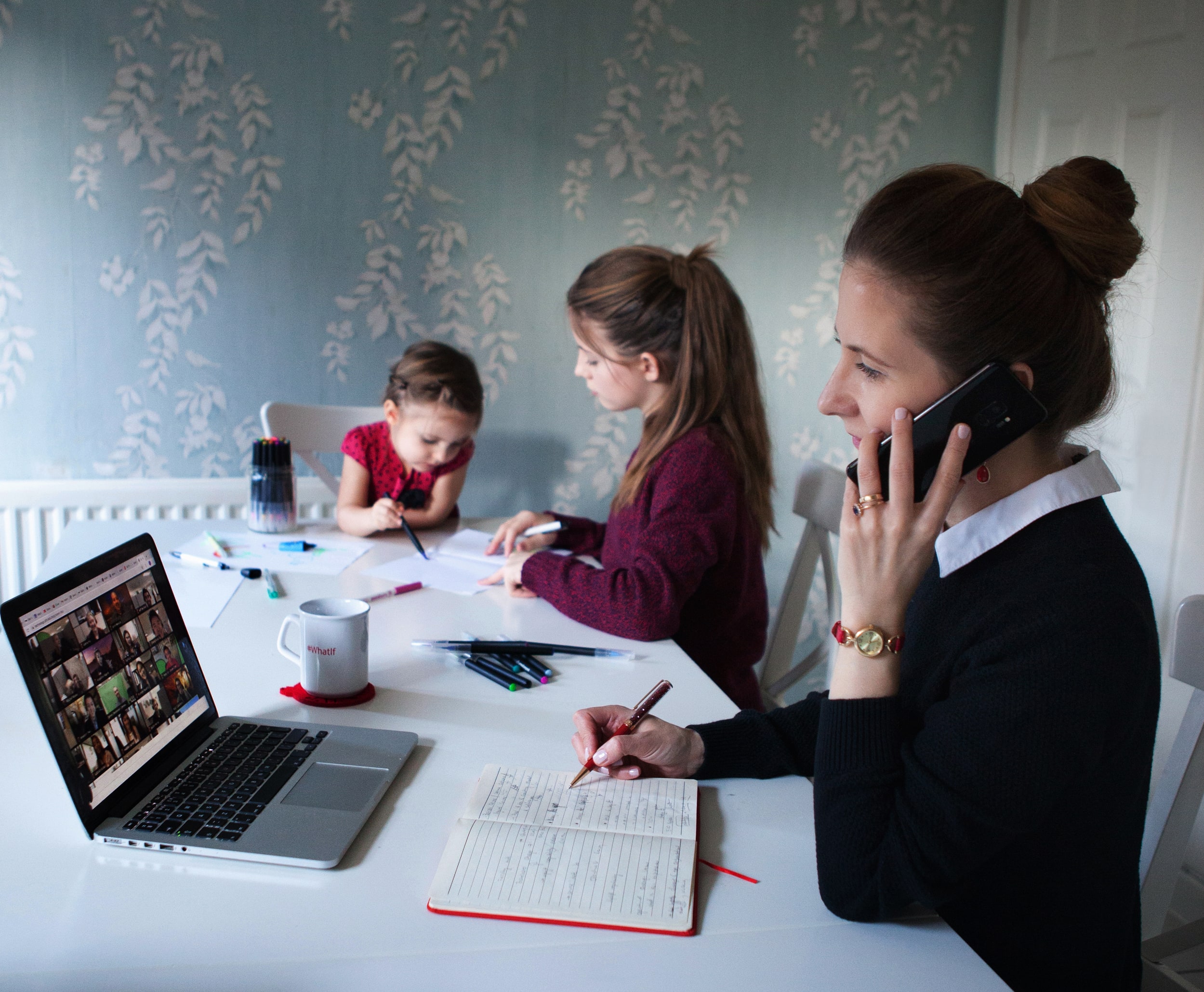 A woman on the phone and on a teams meeting with her children in the background