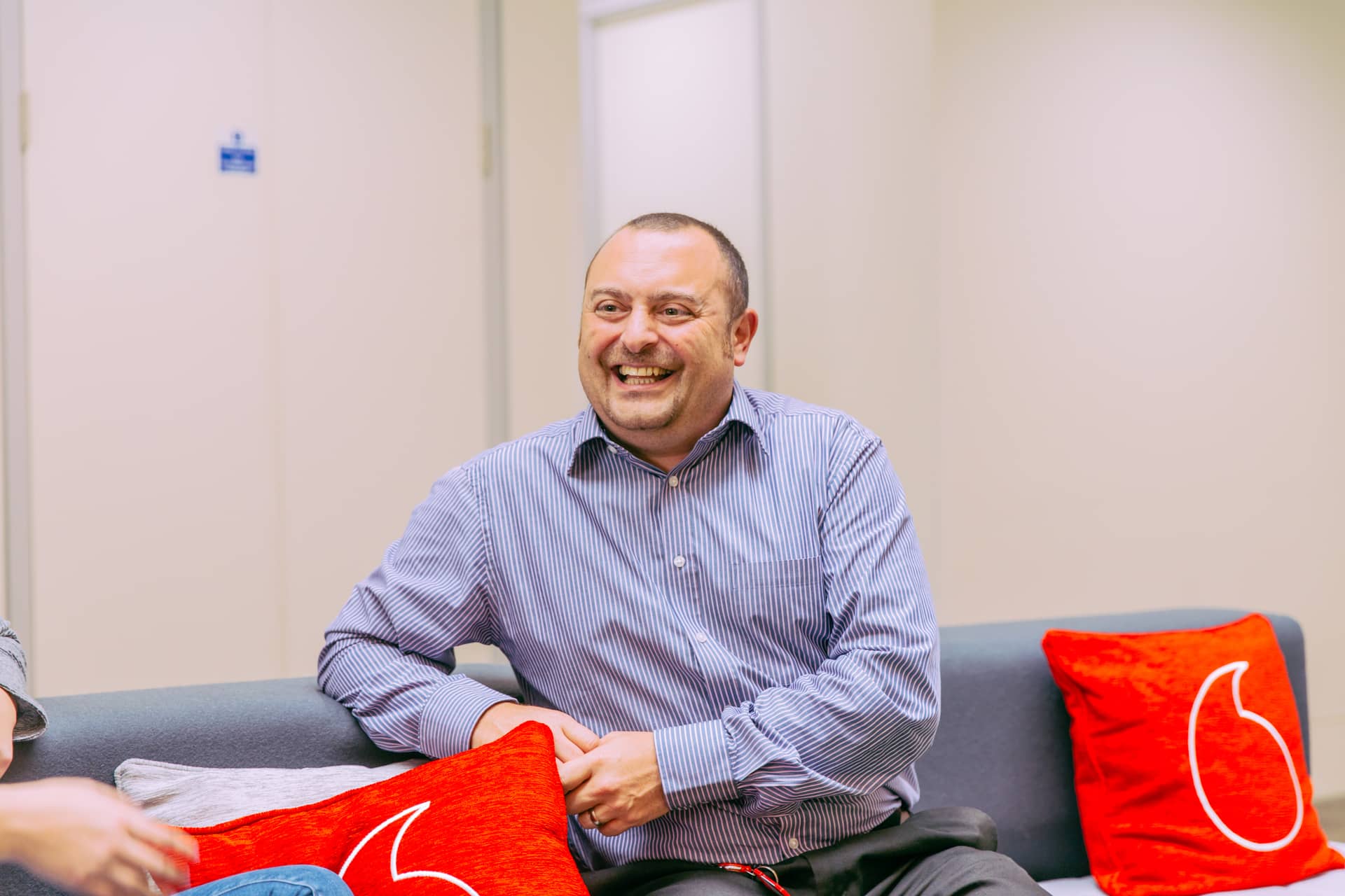 A man smiling on the sofa with Vodafone branded cushions