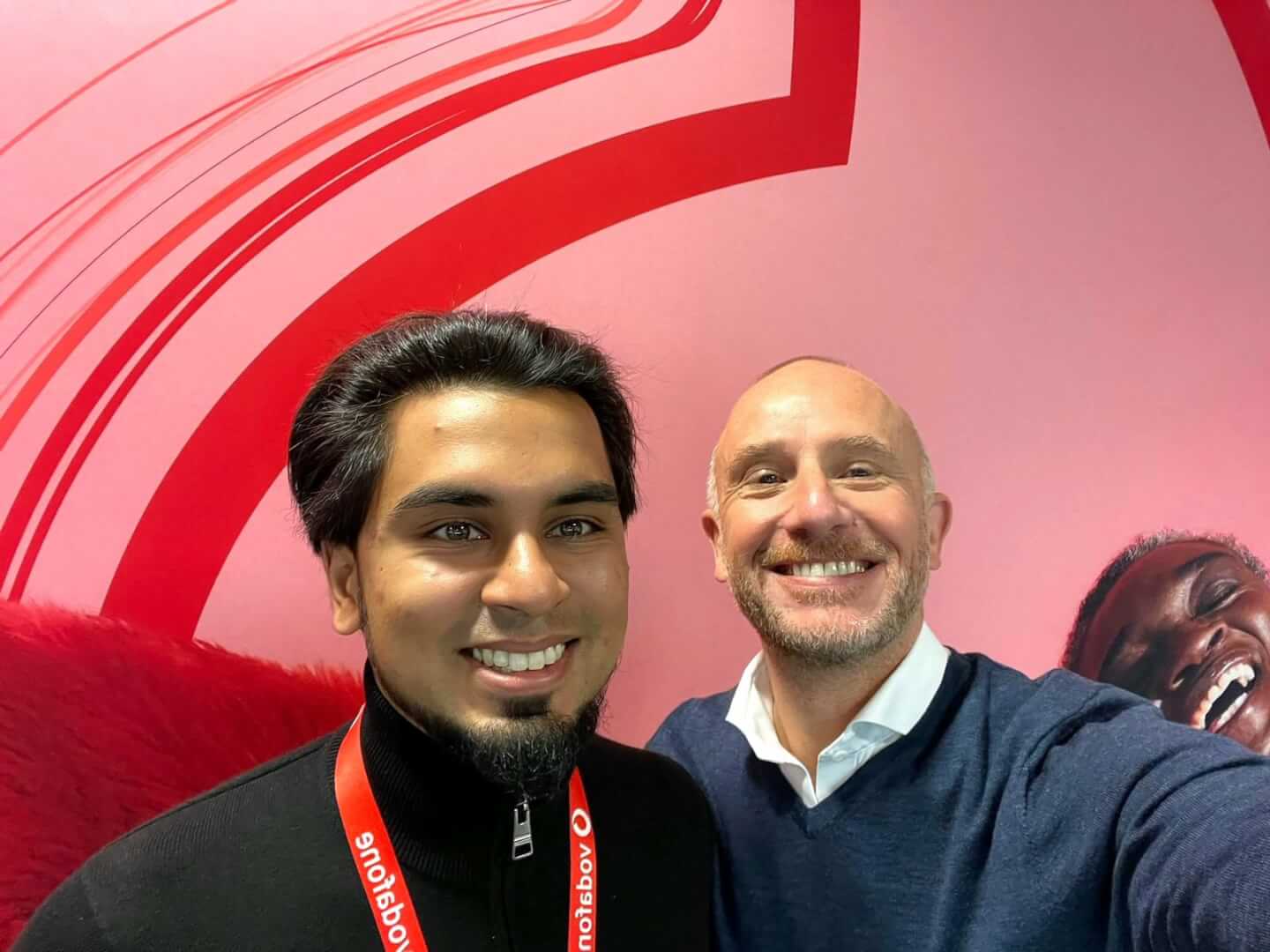 Two people smiling in front of vodafone branding background