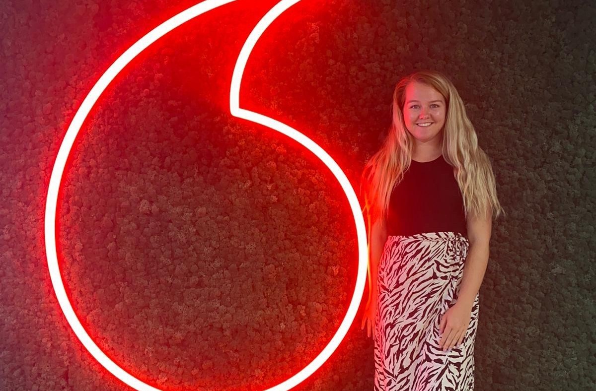 A woman smiling whilst stood next to a Vodafone speechmark logo