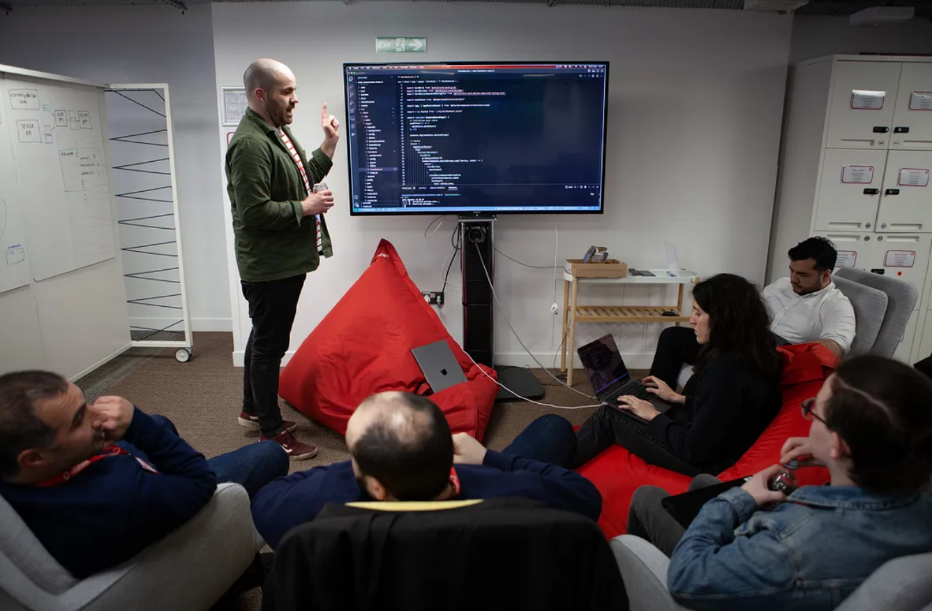 A person presenting to a group of people with a screen of content being shown