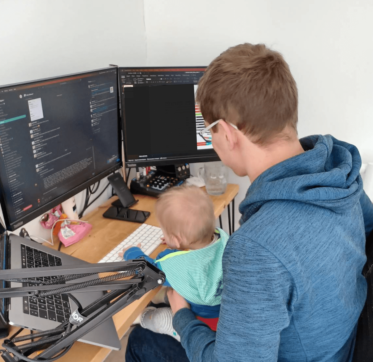 A man and his child sat a desk with monitors and laptops on the desk